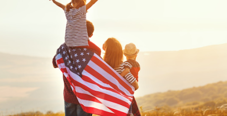 Família com a bandeira dos EUA nas costas observando o sol